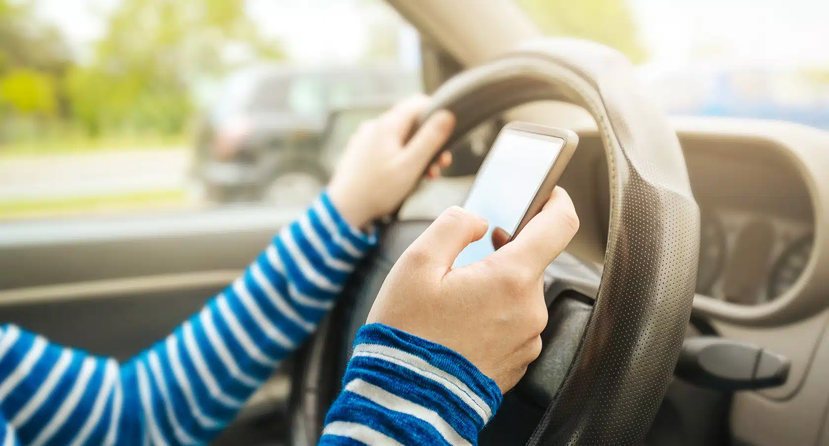 Zwei Hände vor dem Steuer eines Autos bedienen ein Smartphone