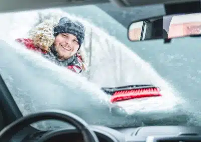 Mann beim Freikratzen der Autoscheibe