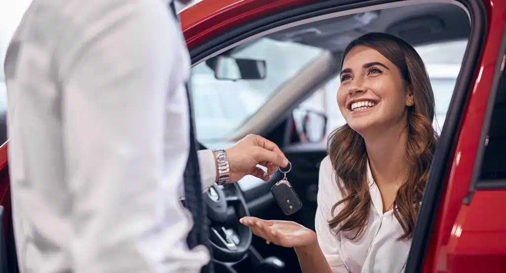 Ein Verkäufer übergibt einer jungen Frau die Autoschlüssel für ein Fahrzeug