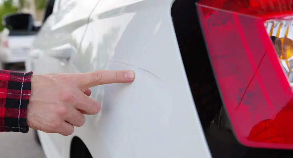 Eine Hand zeigt auf einen Kratzer im Autolack eines Autos