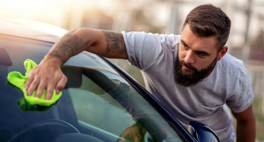 Ein Mann ledert die Scheibe eines Autos mit einem Lappen ab