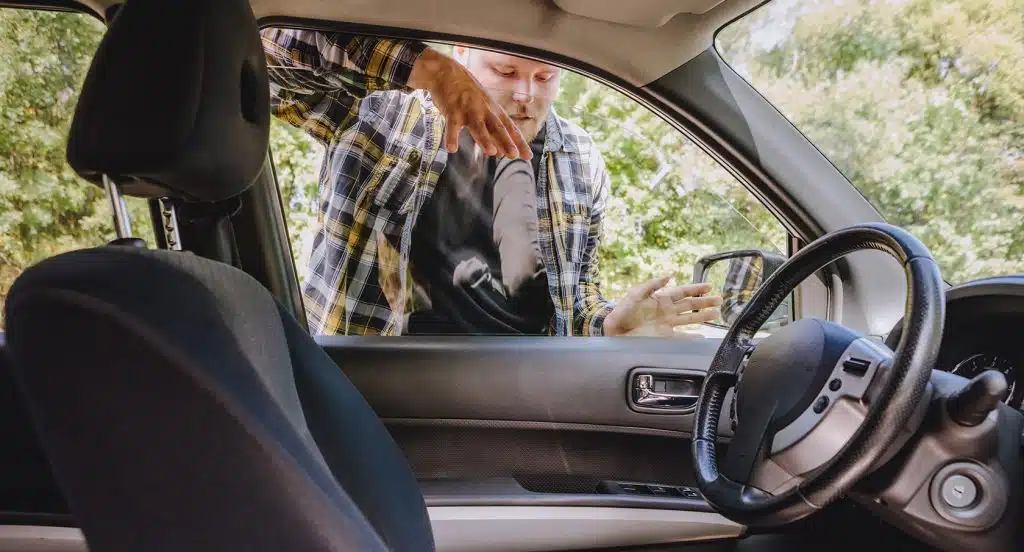 Junger Mann schaut durch eine Autoscheibe auf den Autositz mit einem darauf liegenden Autoschlüssel