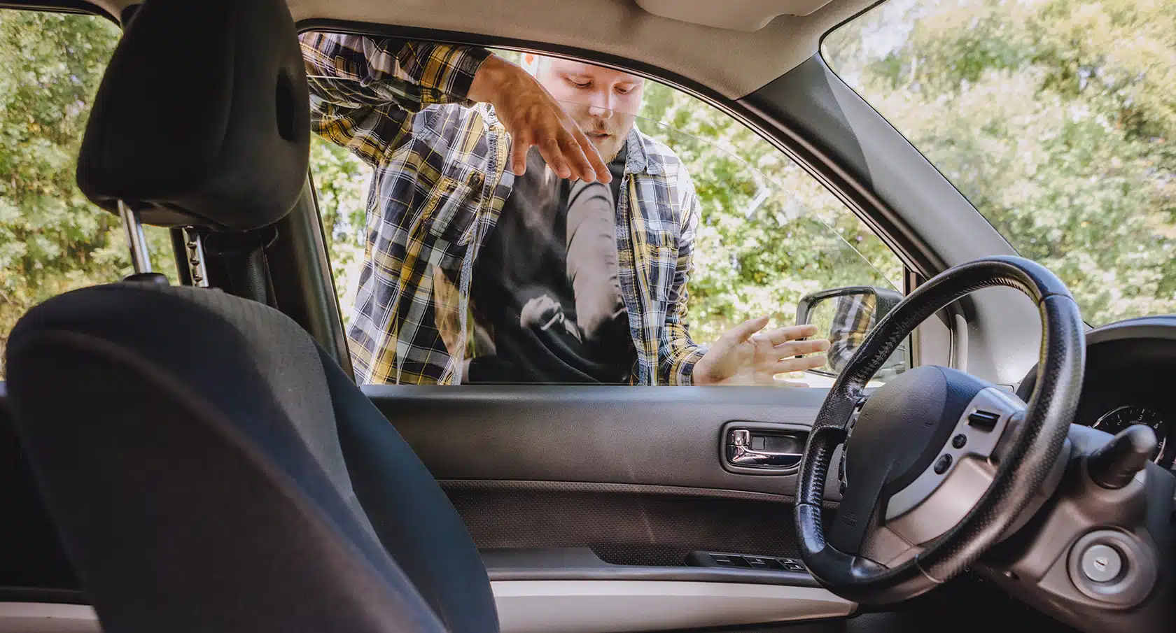 Junger Mann schaut durch eine Autoscheibe auf den Autositz mit einem darauf liegenden Autoschlüssel