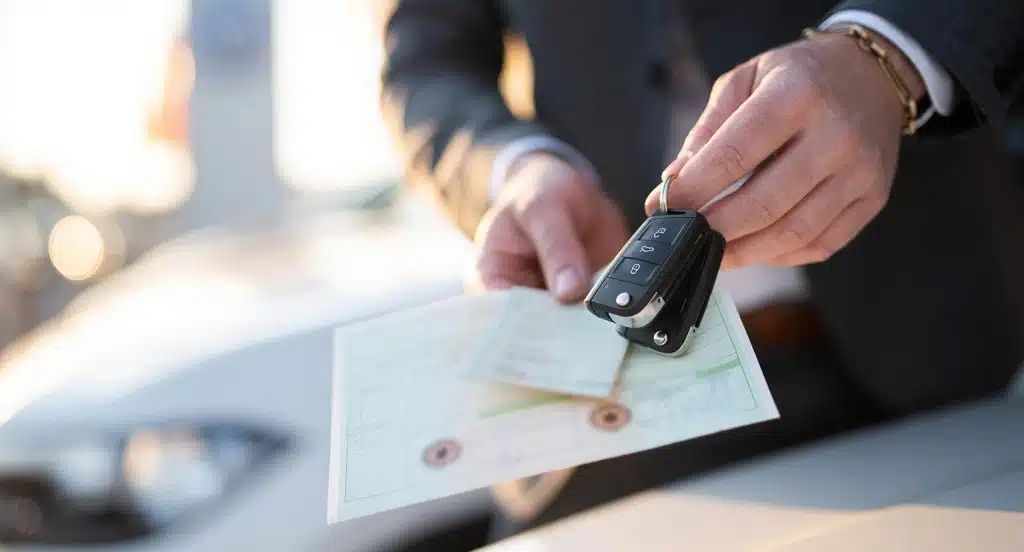 Eine männliche Hand hält seine Fahrzeugpapiere und einen Autoschlüssel in der Hand.