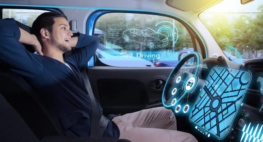 Foto eines Autos von innen, in dem ein Mann sich auf dem Fahrersitz zurücklehnt. Vor ihm sind futuristische Gadgets am Lenker in einem scheinbar autonom fahrenden Auto.
