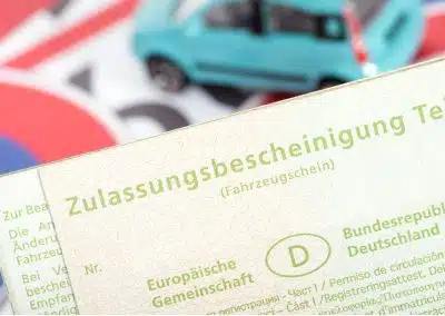 Auto online anmelden: Zulassungsbescheinigung Teil 1 mit Verkehrsschildern und einem Spielzeugauto im Hintergrund