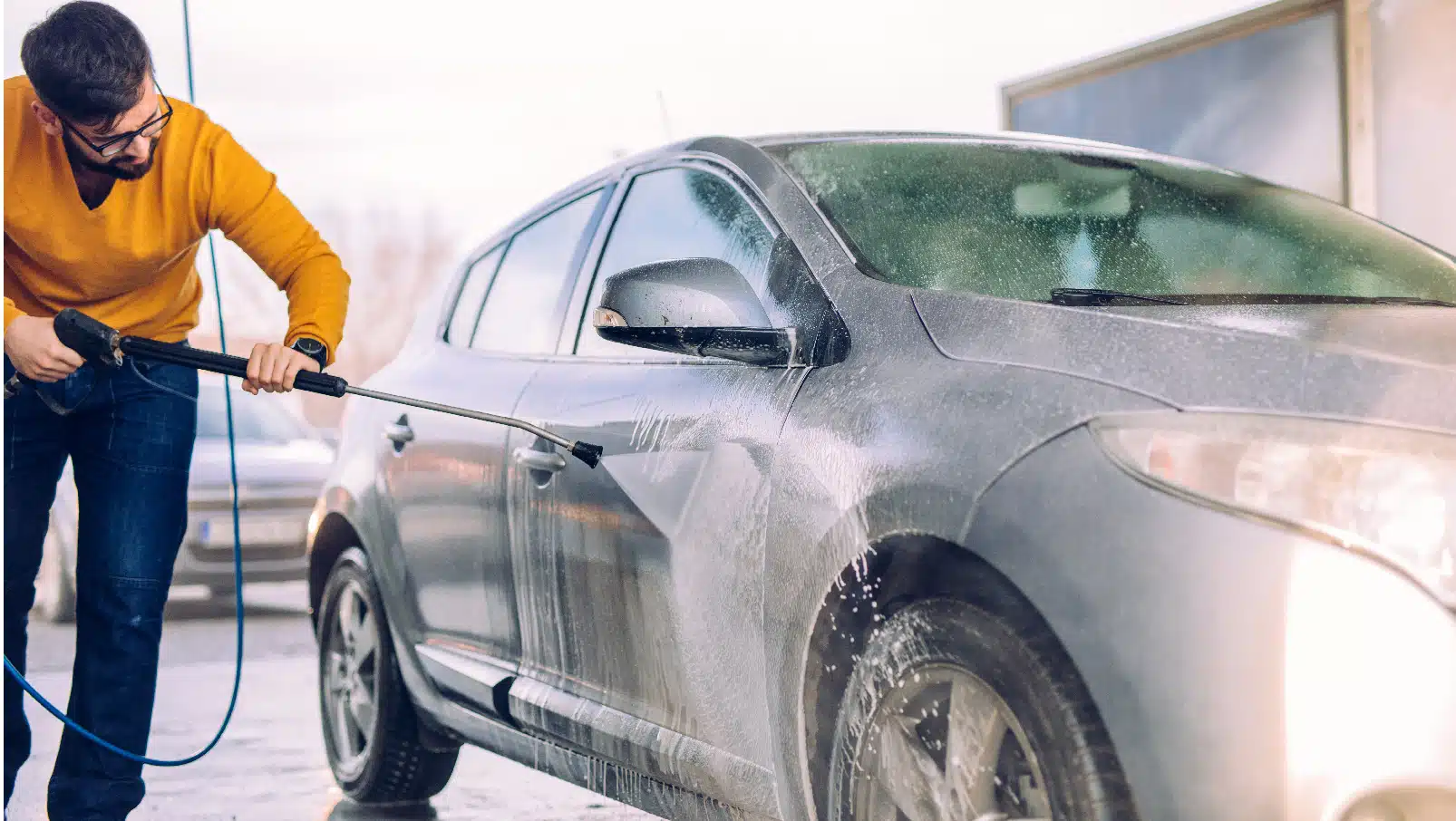 Foto von einem Mann der an einer Waschsäule sein Auto mit einem Hochdruckreiniger abspritzt.
