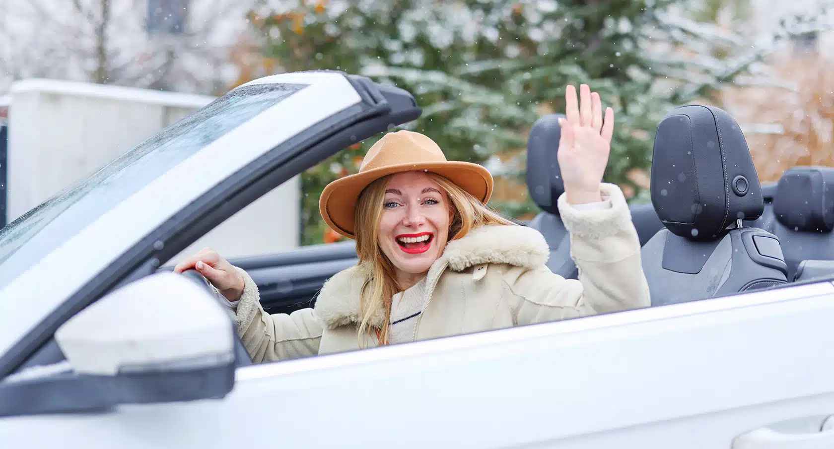Junge Frau mit Hut und Mantel in einem offenen Cabrio