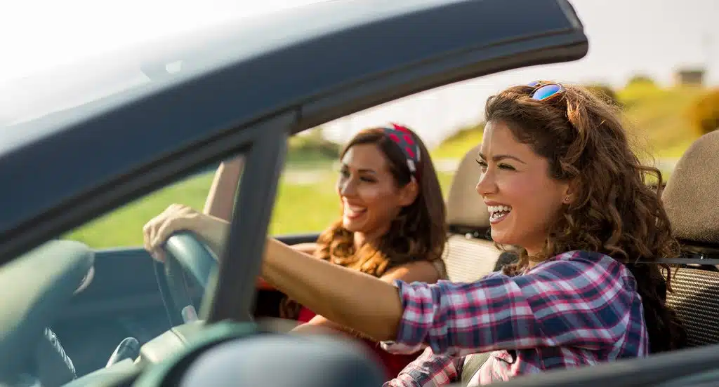 Zwei junge Frauen sitzen in einem offenen Cabrio und lächeln