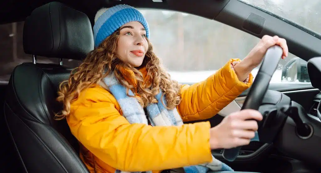 Junge Autofahrerin mit Pudelmütze und Anorak im Auto hinterm Steuer