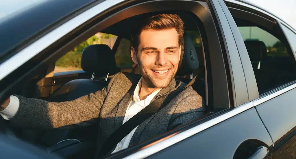 Lächelnder junger Mann schaut aus dem Autofenster eines Firmenwagens