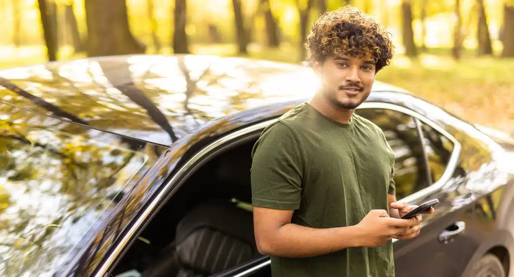 Junger Mann lehnt an einem Auto und lächelt
