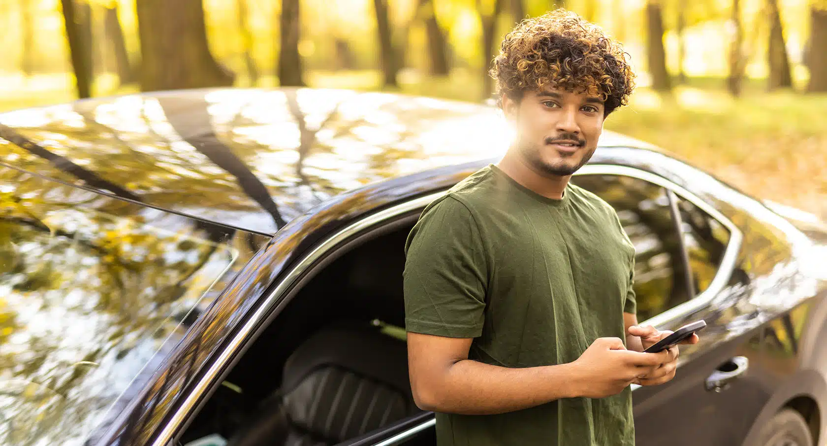 Junger Mann lehnt an einem Auto und lächelt