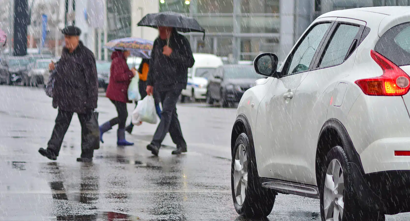 Fußgänger mit Regenschirm überqueren eine Straße vor einem wartenden Auto