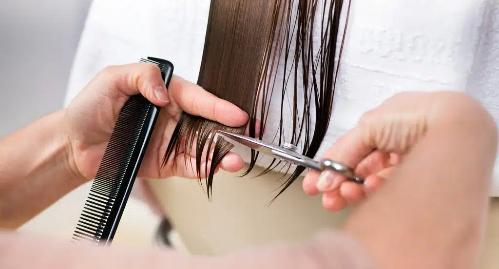 Zwei Hände mit Kamm und Schere schneiden eine Haarsträhne