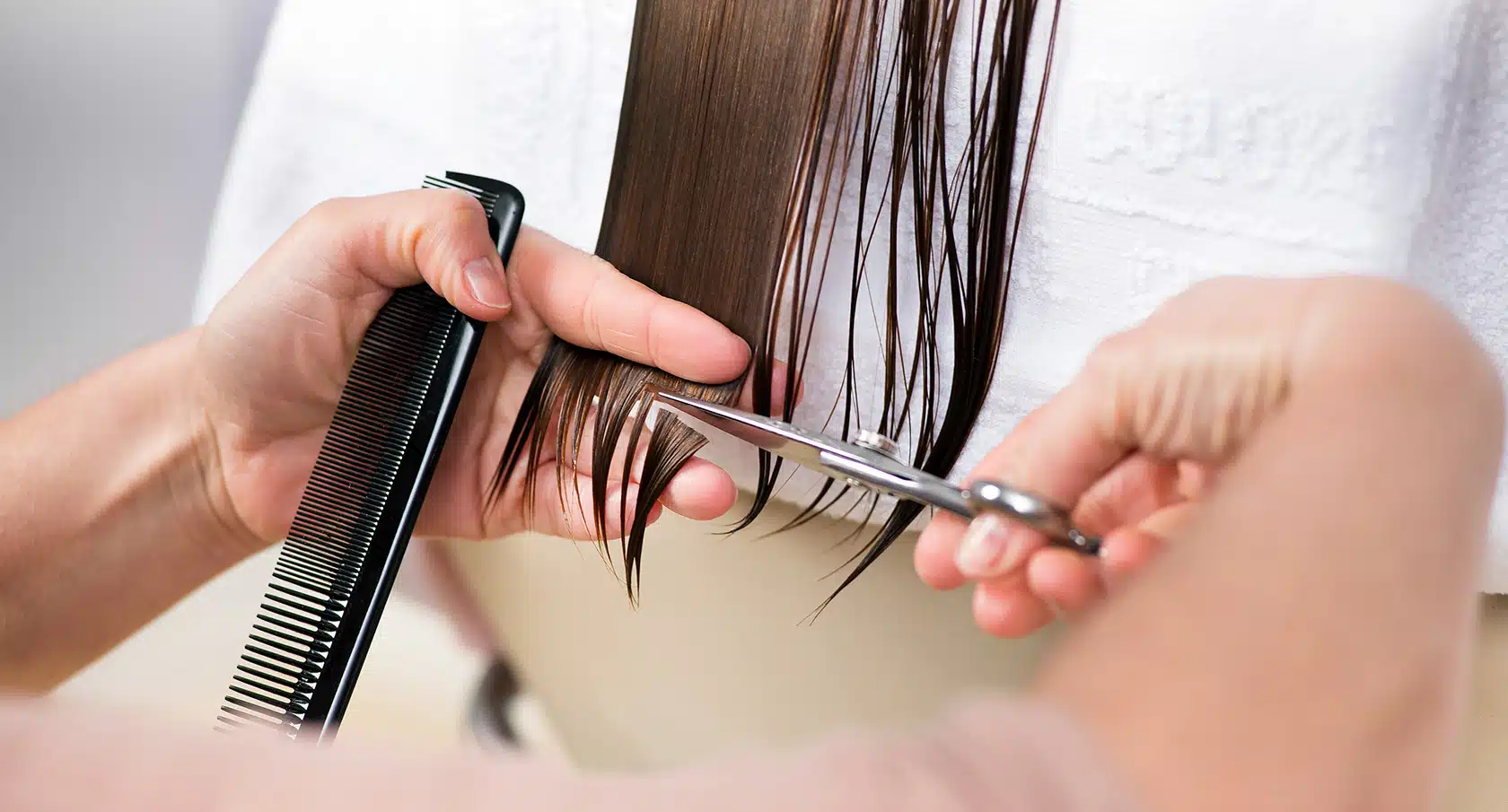 Zwei Hände mit Kamm und Schere schneiden eine Haarsträhne
