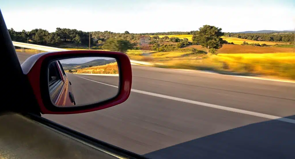 Blick auf eine Landstraße aus dem Auto in den Seitenspiegel