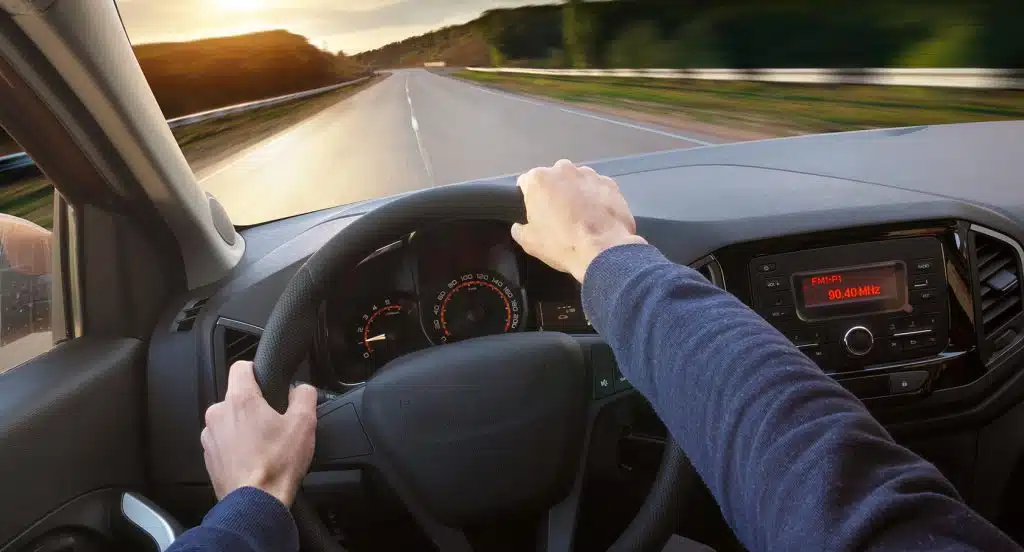 Zwei Hände Am Lenkrad vor der Aussicht durch eine Autoscheibe auf die Straße