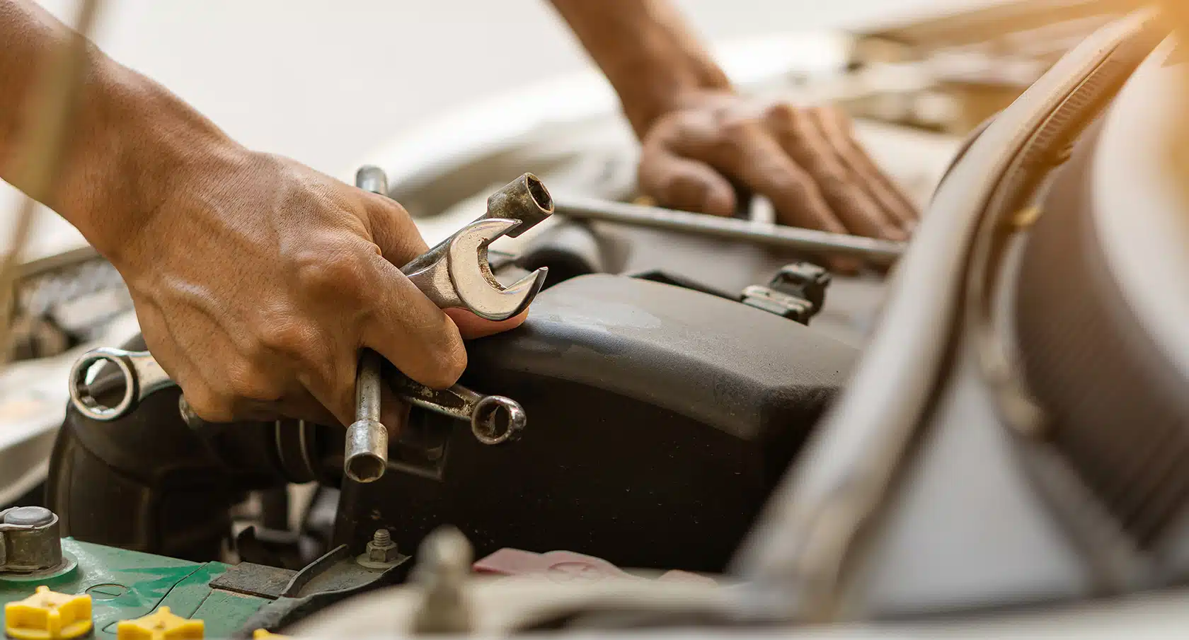 Eine Hand hält ein Werkzeug vor einem geöffneten Motorraum