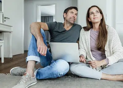 Pärchen sitzt auf dem Boden mit einem Laptop auf dem Schoß