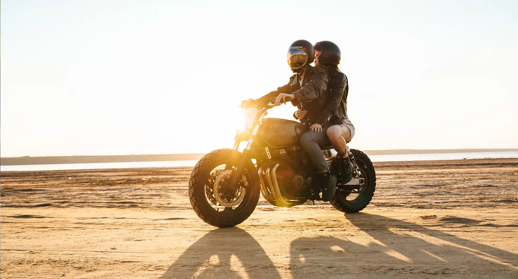 Motorradfahrer und Beifahrer fahren auf einer Maschine am Strand entlang