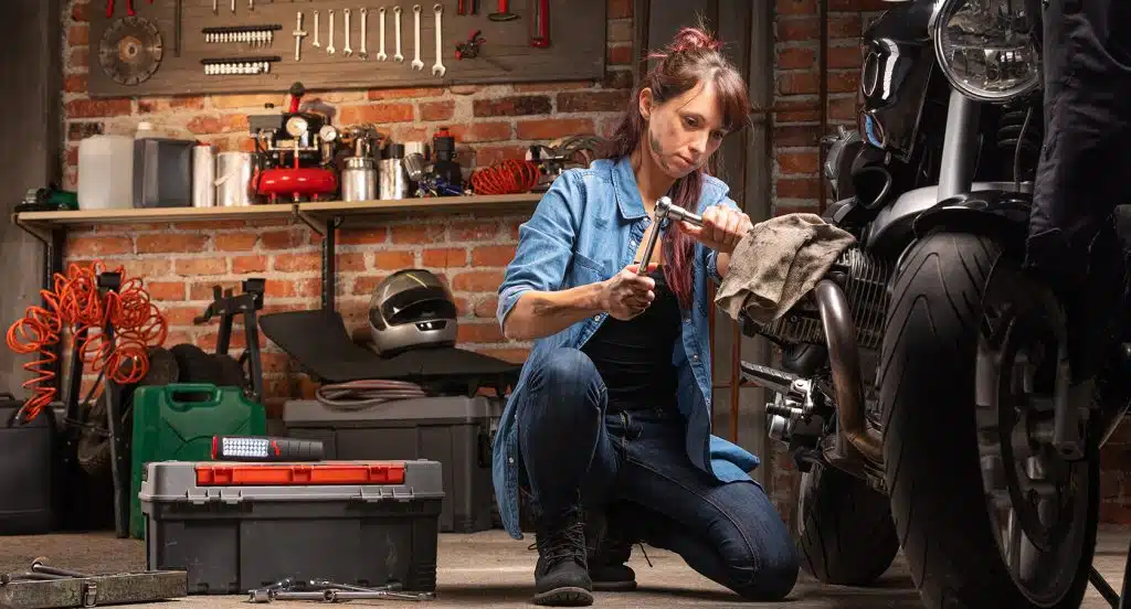 Junge Frau bastelt in der Garage an einem Motorrad