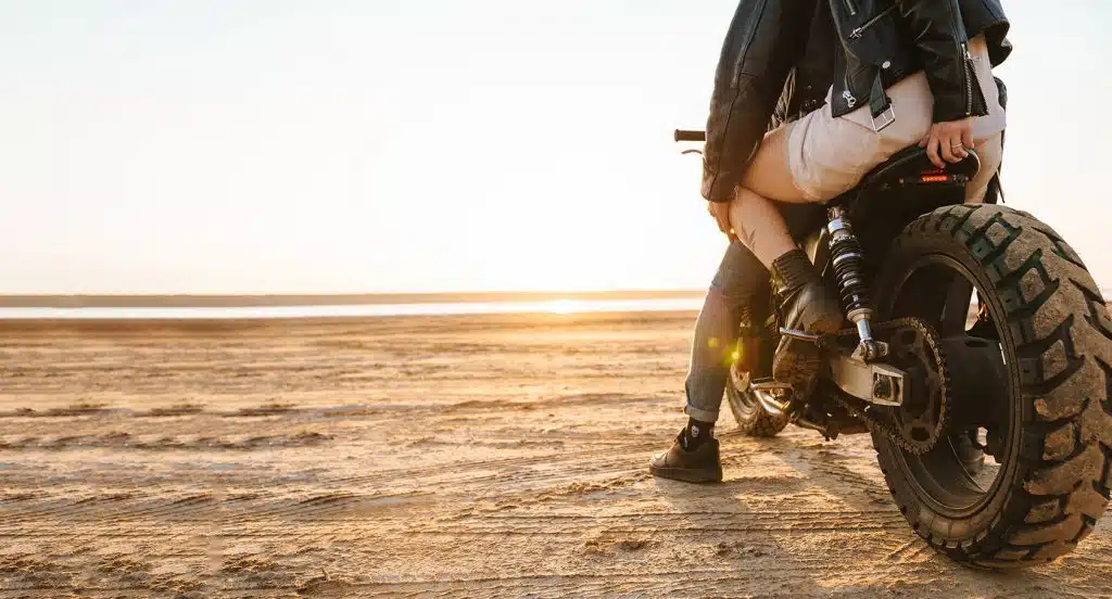 Motorrad mit Fahrer und Beifahrer steht an einem Strand