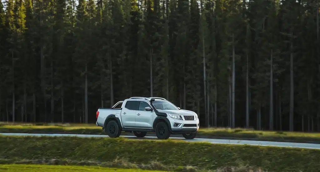 Ein Pick-Up fährt vor einem Wald auf einer Landstraße