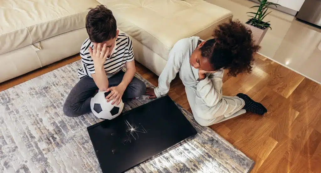 Zwei Kinder mit einem Fussball in der Hand sitzen vor einem zerbrochenen Fernseher