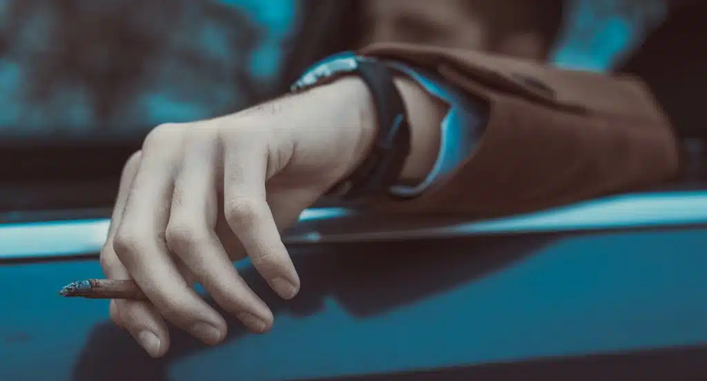 Eine Hand mit einer Zigarette hängt aus dem Fenster eines Autos heraus