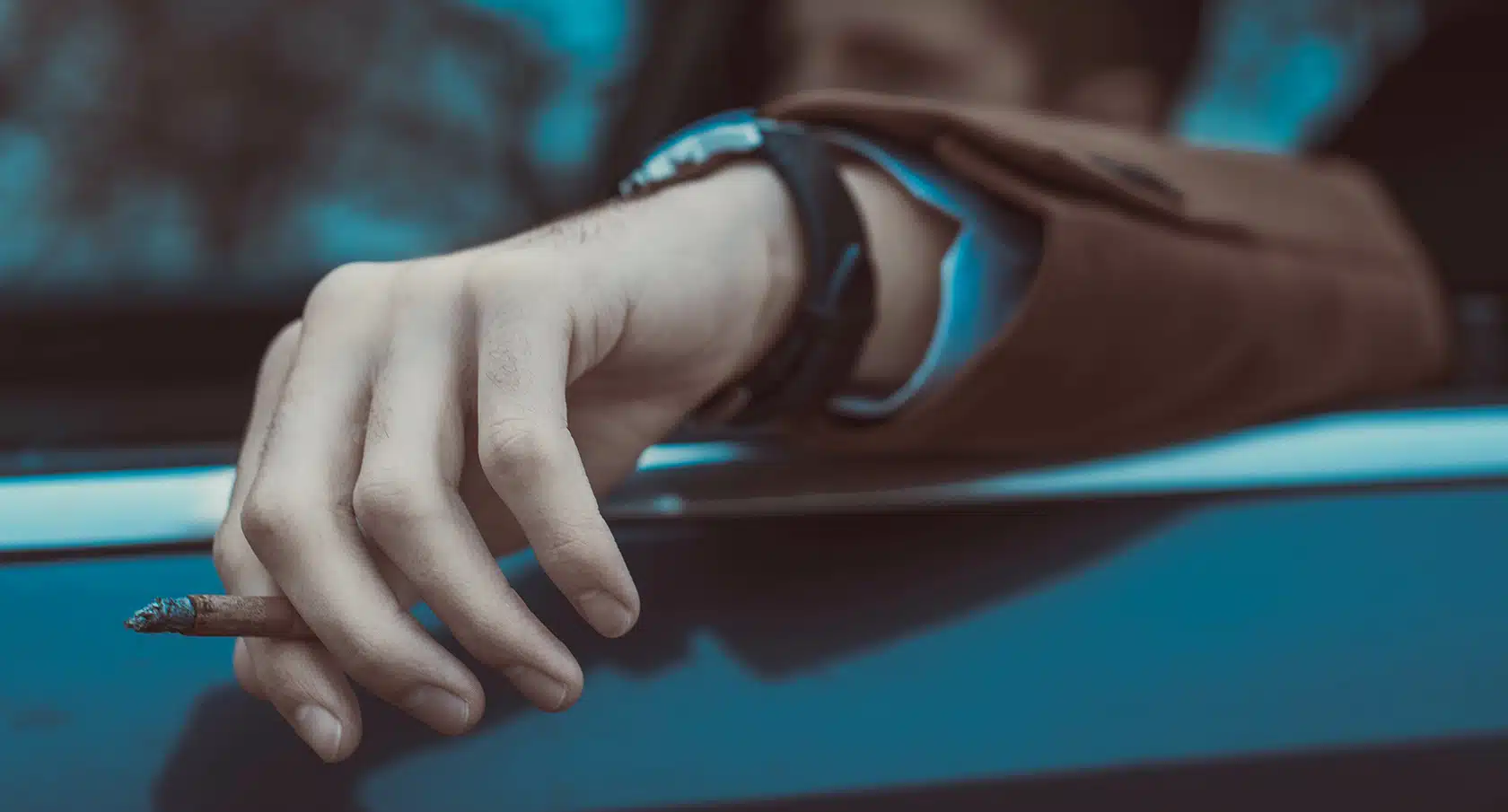 Eine Hand mit einer Zigarette hängt aus dem Fenster eines Autos heraus