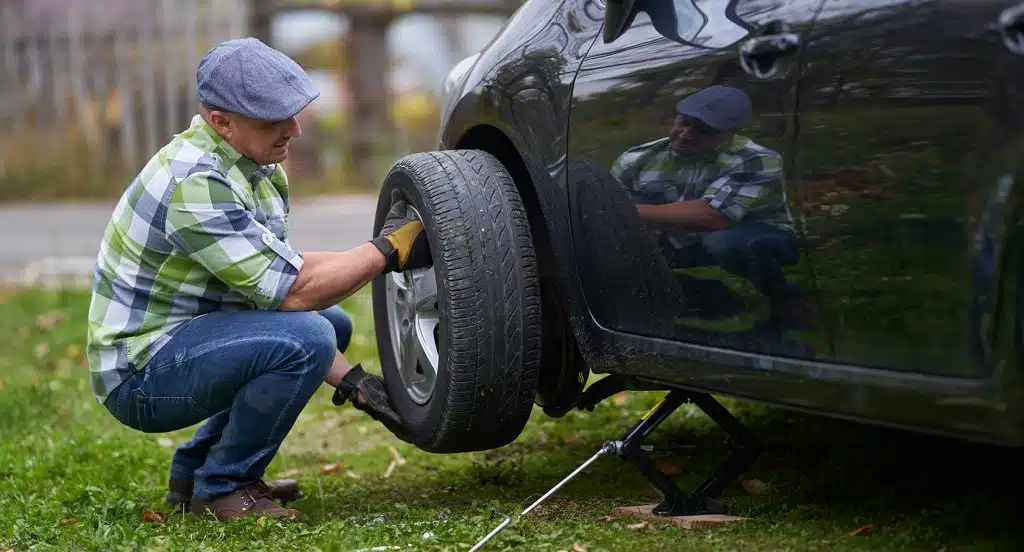 Junger Mann beim Reifenwechsel an einem Auto