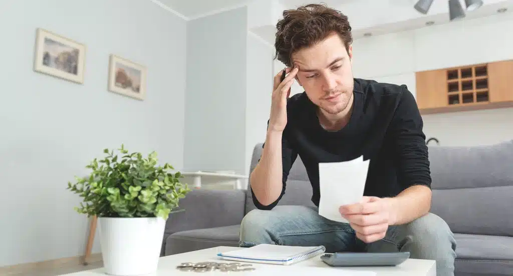 Junger Mann sitzt auf der Couch und studiert ein Dokument in seiner Hand