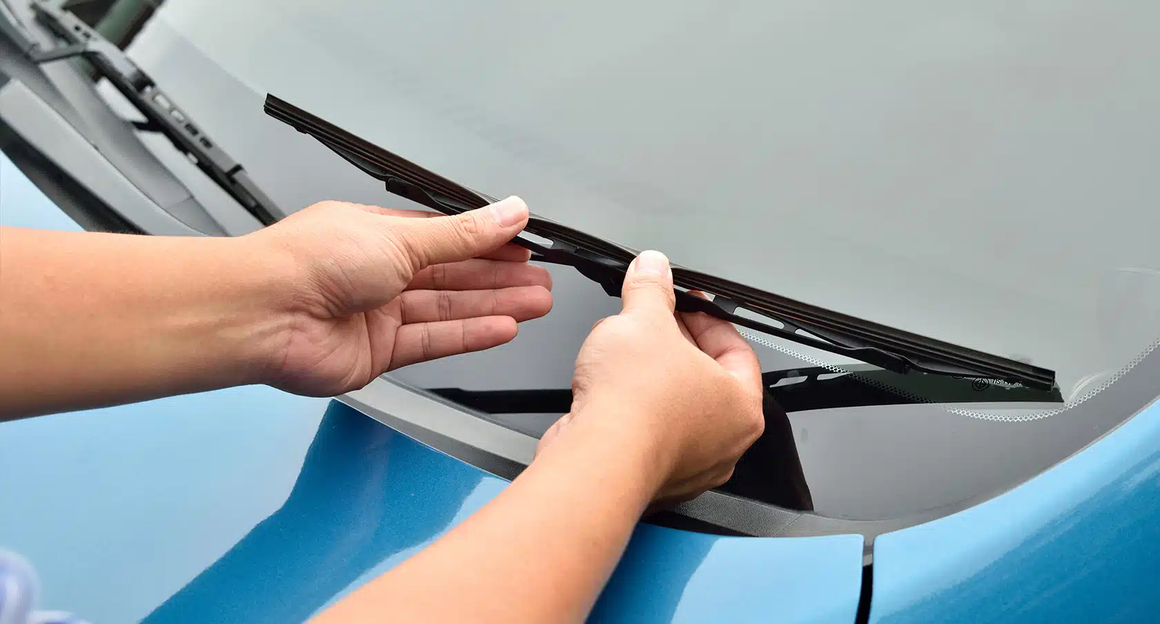 Zwei Hände wechseln einen Autoscheibenwischer