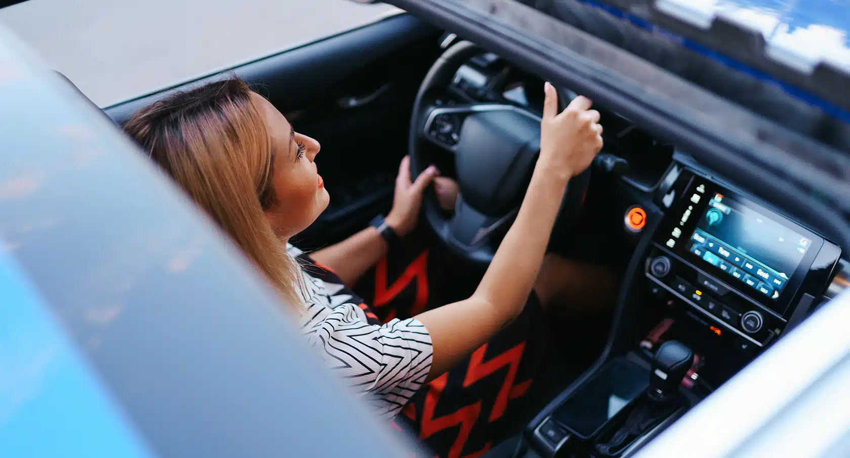 Geöffnetes Panoramadach eines Auto von oben mit Blick auf eine junge Frau am Steuer