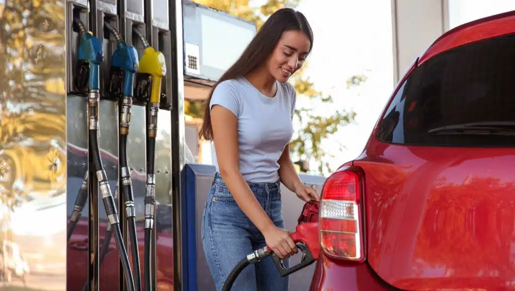 Beim Tanken sparen: Junge lächelnde Frau tankt ihr Auto an einer Tankstelle auf