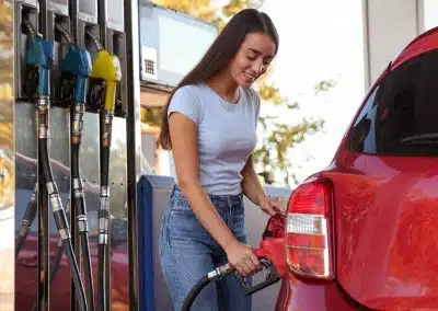 Beim Tanken sparen: Junge lächelnde Frau tankt ihr Auto an einer Tankstelle auf