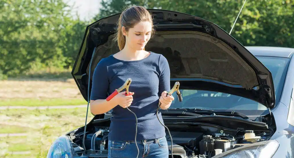 Frau vor einem Auto mit Starthilfekabel in der Hand