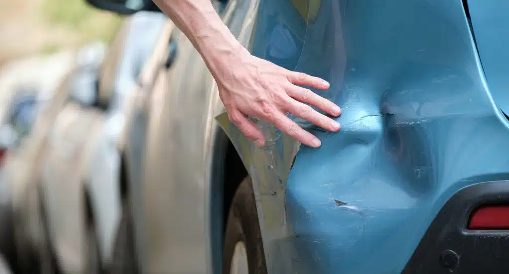 Eine Hand befühlt eine Beule im Autolack