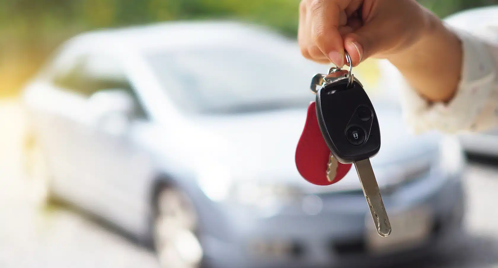 Eine Hand hält einen Autoschlüssel vor ein unscharfes Fahrzeug