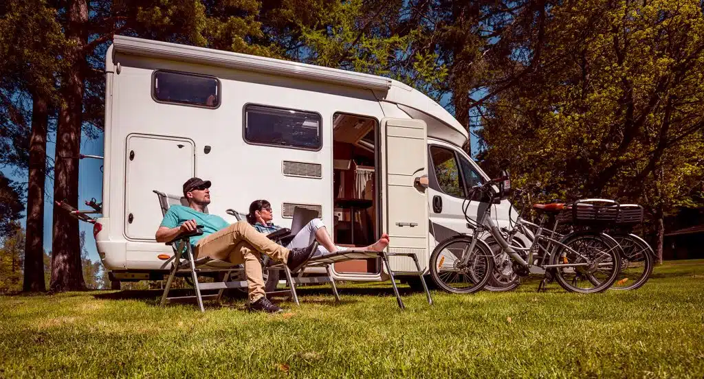 Junges Pärchen sitzt vor einem Wohnmobil im Grünen