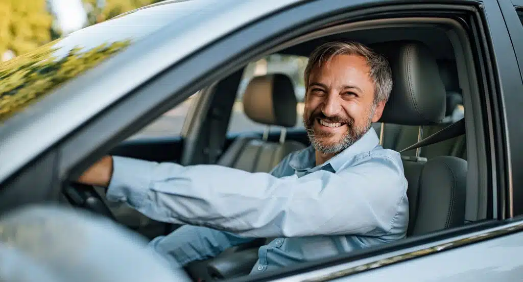 Lächelnder Autofahrer schaut durch das Fahrerfenster eines Autos