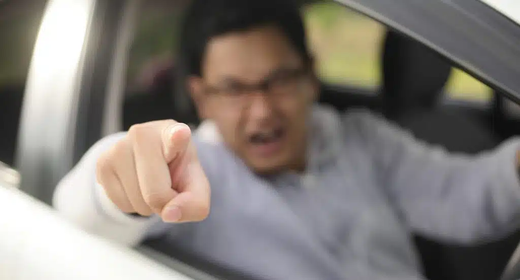 Aggressiver Autofahrer zeigt mit dem Finger aus dem Fenster eines Autos
