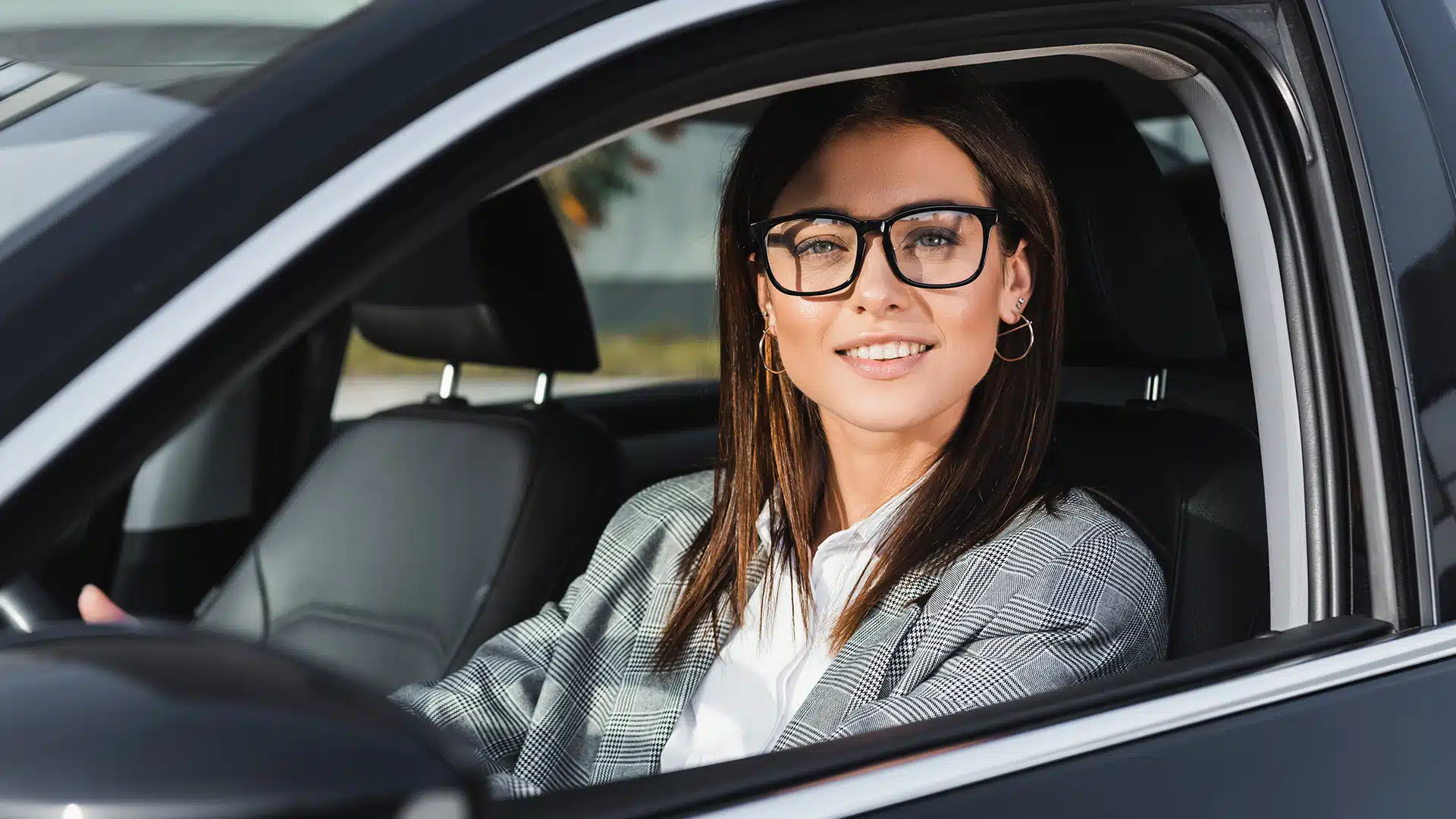 artikelbild-blog-Gute Fahrer-AdobeStock_396600359 Frau mit Brille sitz im Auto, Fenster heruntergerollt, und lächelt freundlich in die Kamera.