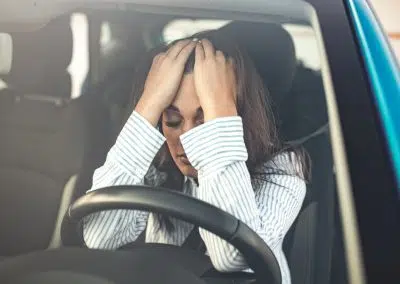 Frau sitzt in Auto und hält sich die Hände vors Gesicht