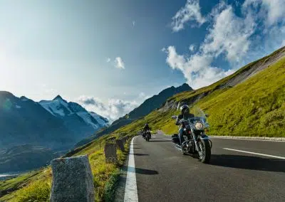 Motorradfahrer fährt eine Straße an einem Hügel entlang. Im Hintergrund sind Berge.