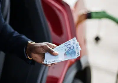 Mann hält Geldscheine vor E-Auto in der Hand