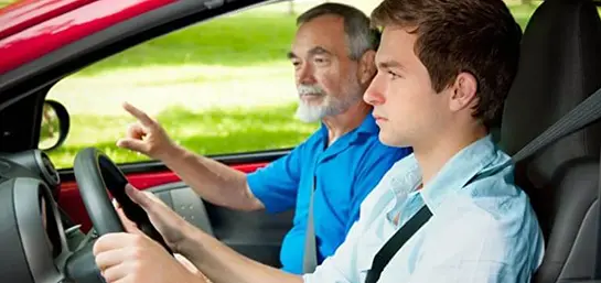 Fahrlehrer sitzt mit Fahrschüler im Auto und gibt Anweisungen
