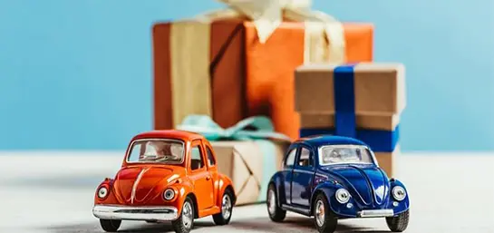 Zwei Miniaturautos vor verpackten Geschenken