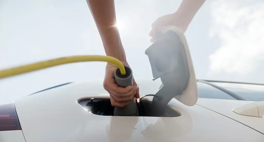 Eine Hand steckt ein Elektro-Ladekabel in ein Auto